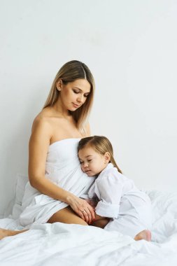 Bir güzel hamile anne ve kızı beyaz yatakta oynamaya 