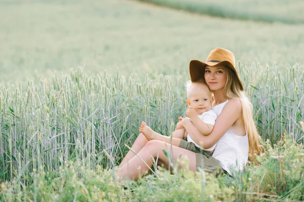 Egy fiatal anya és a kis gyermek ül a búza közelében egy — Stock Fotó