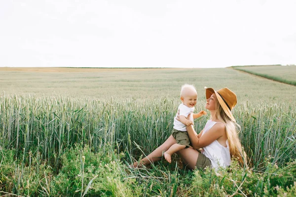 A young mother and her little child sitting near the wheat on a — Stock Photo, Image