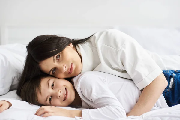 Mulher bonita e seu filho pequeno bonito estão deitados na cama um — Fotografia de Stock