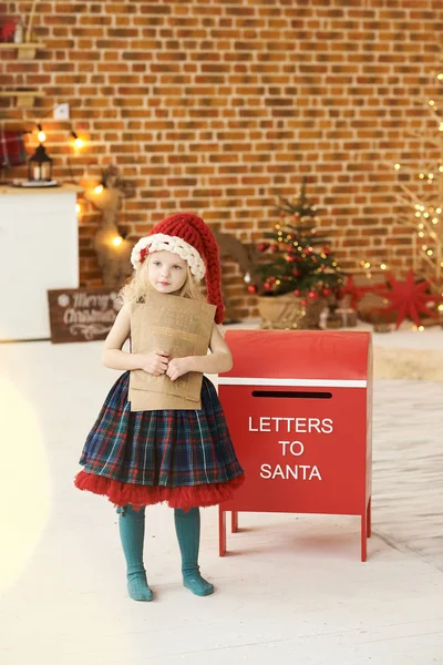 Una niña con un sombrero de Navidad envía una carta a Santa adentro. — Foto de Stock