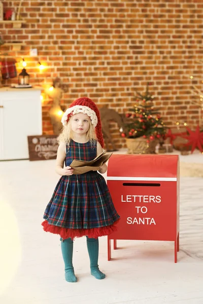 Una niña con un sombrero de Navidad envía una carta a Santa adentro. — Foto de Stock