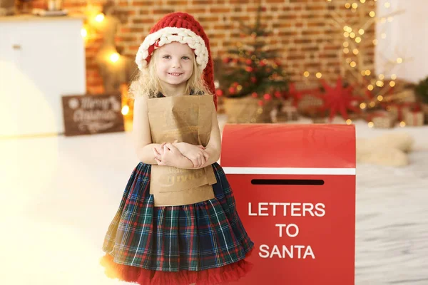 Una niña con un sombrero de Navidad envía una carta a Santa adentro. —  Fotos de Stock