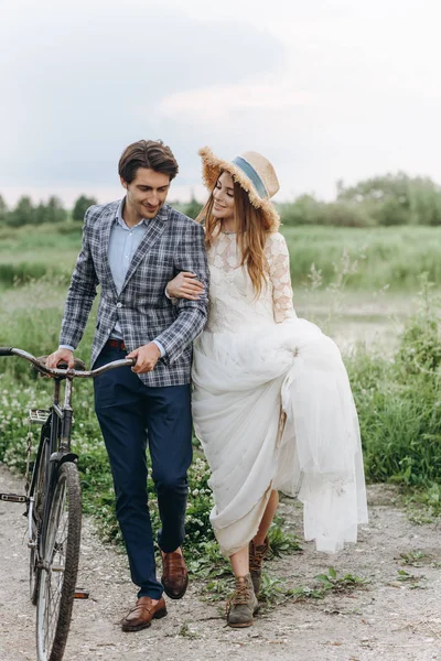 Casal jovem bonita noiva e noivo andando em um campo com um — Fotografia de Stock