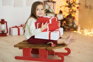 Kırmızı kızaklı küçük bir kızın portresi ve üstünde bir hediye.