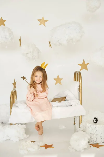 Little princess with a magic wand on  bed in a cloud on a white background