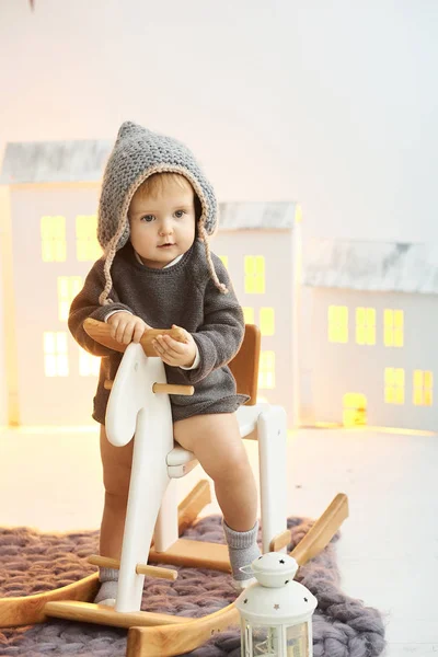 Małe dziecko siedzi na drewnianej łyżwach na tle zabawki hou — Zdjęcie stockowe