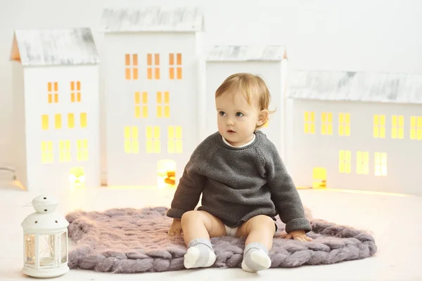 Un niño pequeño se sienta en una alfombra gris sobre un fondo de un juguete ho —  Fotos de Stock