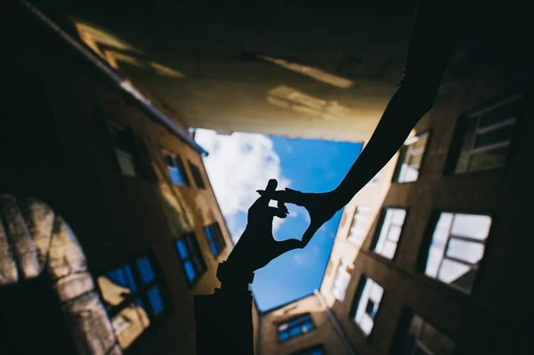 Le mani di un uomo e una donna fanno una forma di cuore su uno sfondo di cielo blu tra le case. — Foto Stock
