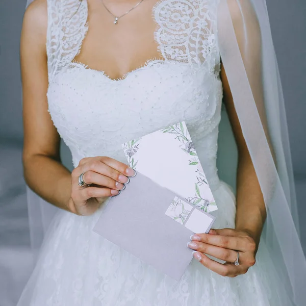 Close up of faceless girl in beautiful white wedding dress holding an envelope with a blank postcard. — Stock Photo, Image