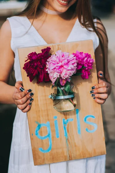 Mädchen hält ein Holzbrett mit der Aufschrift Girla und befestigt daran ein Glas mit Pfingstrosen. — Stockfoto