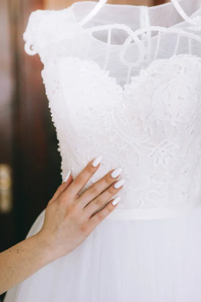 Primer plano de la mano novias toca un hermoso vestido de novia blanco que cuelga de una percha blanca. —  Fotos de Stock