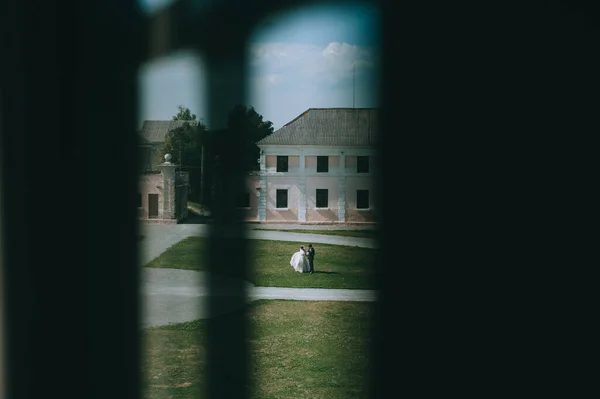 Düğün çifti eski evlerin arasında duruyor, açık bir antika pencereden bakıyorlar.. — Stok fotoğraf