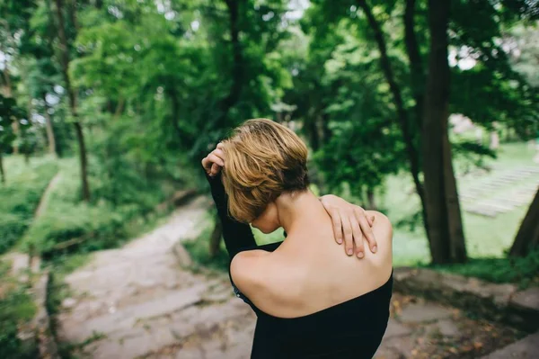 Zadní pohled na ženu s krátkými vlasy objímající se na pozadí zelené přírody v parku. — Stock fotografie