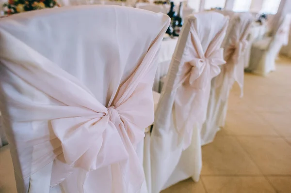 Fila de hermosas sillas decoradas con tela y arcos de delicado color rosa en la sala de bodas. —  Fotos de Stock