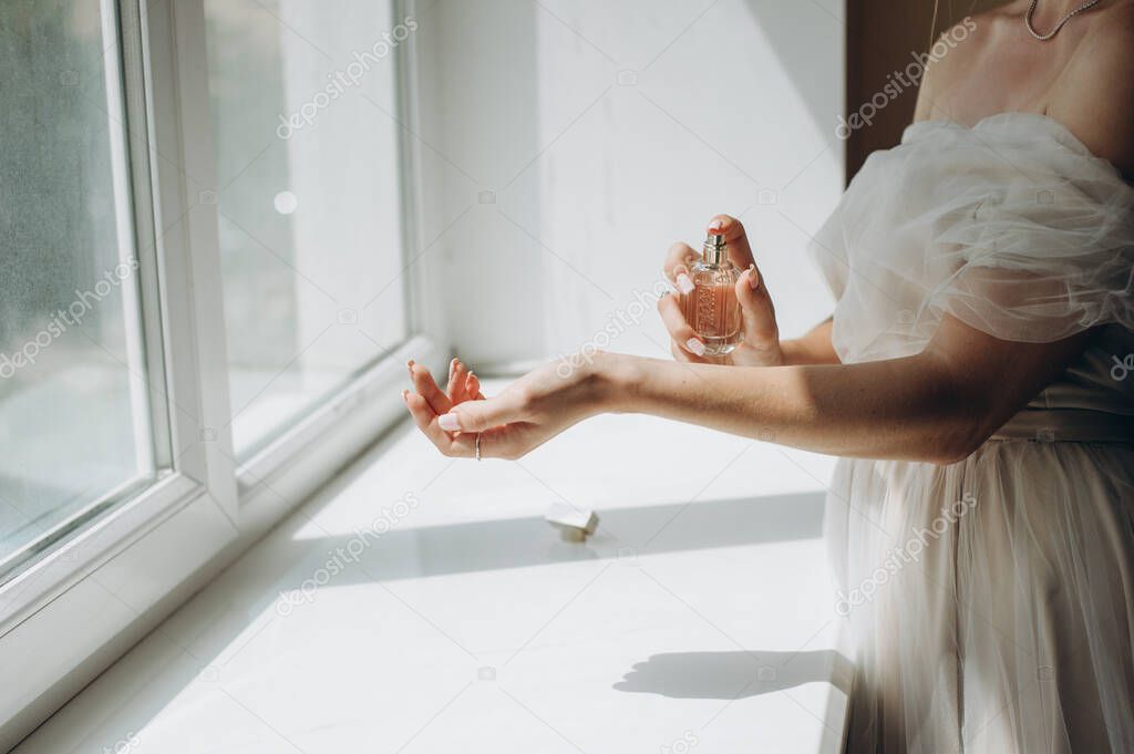Luxurious faceless groom sprays elegant perfume on his arm in the room by the window.