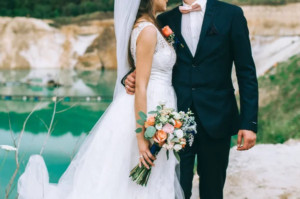 Casado recentemente casal amoroso com anéis em suas mãos e um buquê da noiva abraçando. — Fotografia de Stock