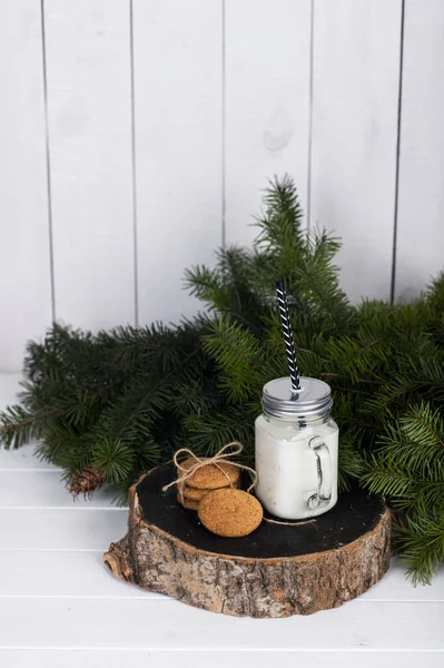 Bougie dans un bocal en verre et biscuits sur une bûche en bois près d'une branche d'épinette sur un fond blanc. — Photo