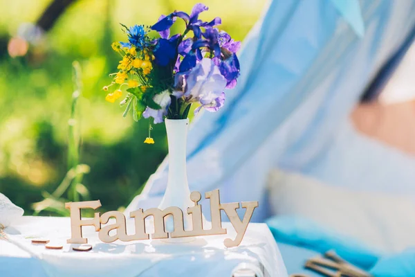 Großaufnahme der hölzernen Inschrift Familie steht auf dem Tisch neben weißer Vase mit frischen Wildblumen. — Stockfoto