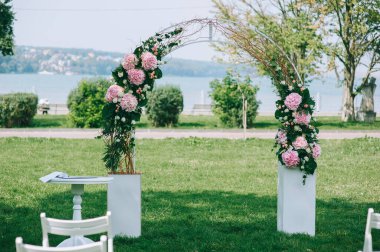 Geniş yeşil çimlerde pembe ortanca çiçeklerinden, güllerden ve yeşillikten yapılmış zarif bir düğün kemeri..