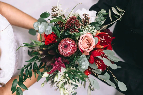 Beau bouquet de mariage dans les tons rouges dans les mains de la mariée dans une robe de mariée. — Photo