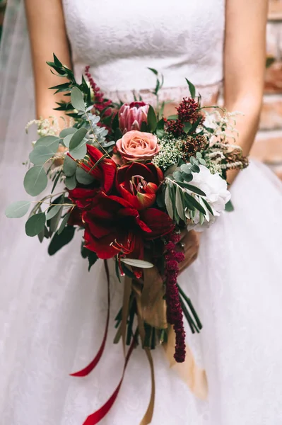 Belo buquê de casamento em tons vermelhos nas mãos da noiva em um vestido de noiva. — Fotografia de Stock