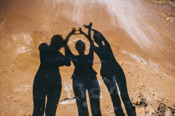 Καλοκαιρινή διασκέδαση Σκιά μιας όμορφης οικογένειας που διασκεδάζει στην παραλία το ηλιοβασίλεμα δίπλα στη θάλασσα. — Φωτογραφία Αρχείου