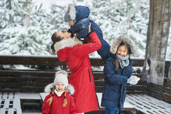 Eine junge Mutter mit ihren drei Kindern vergnügt sich beim Schneeballspielen im Freien in der Nähe des Hauses — Stockfoto