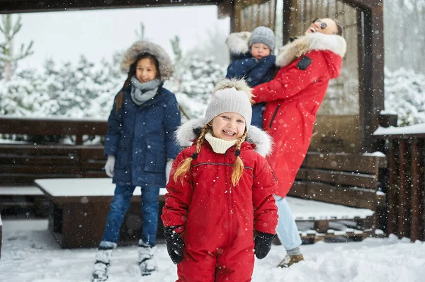 木の子供たちと一緒にいる若い母親は、家の近くで雪玉を楽しんで遊んでいます — ストック写真