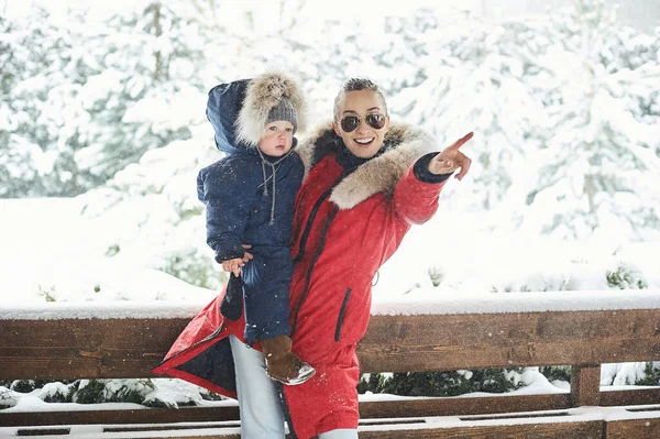 A Beautiful young mother with children in winter, near the house with a snow covered christmas trees — Stock Photo, Image