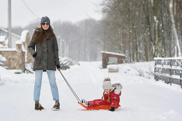 A young beautiful mom sledges her baby — Stock Photo, Image