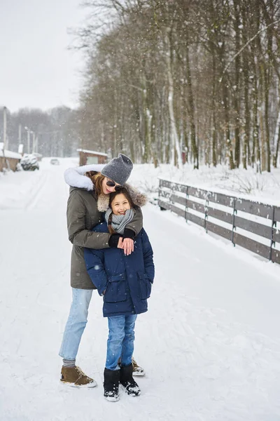 A portret of beautiful young caucasian mother with her children in winter near the house with a snow covered christmas trees in a background — Stock Photo, Image