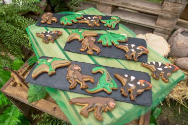 Homemade gingerbread cookies with the handmade icing decoration as funny dinosaurs. Wooden surface. clipart