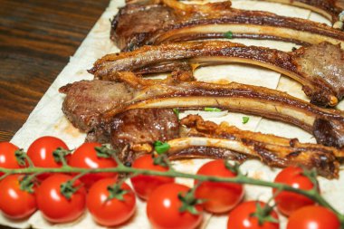 Baharatlı, ızgara pirzola. Barbekü, acı biber ve taze domatesle servis edilir. Eski bir ahşap kesim tahtasının üzerinde..