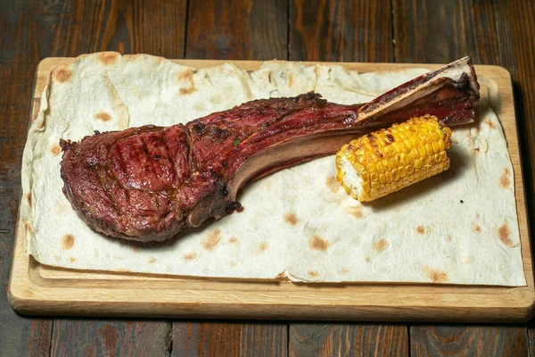 Filetes Tomahawk recién asados en tabla de cortar de madera con maíz —  Fotos de Stock