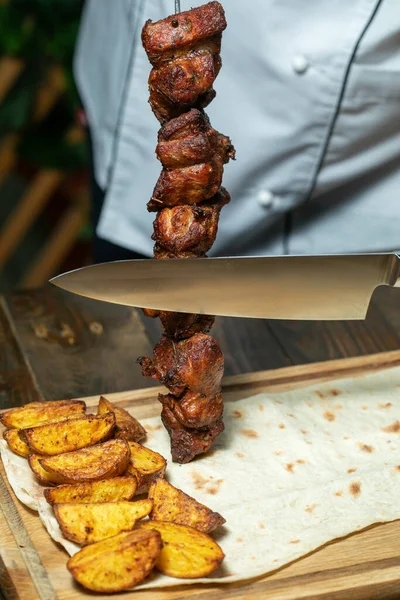 Grilled meat with potatoes. the chef cuts the kebab with a knife.