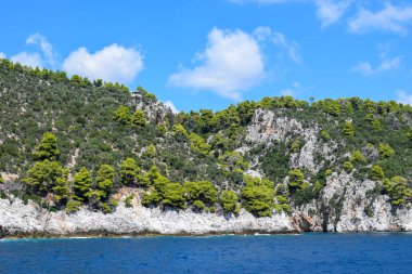 Yeşillik, kalın ormanlık ve turkuaz tropikal sularla dolu güzel bir Yunan adası manzarası. Dağlar, yoğun yeşil ormanlar, beyaz kayalar ve berrak mavi sular, cennet gibi seyahat noktalarını oluşturur..