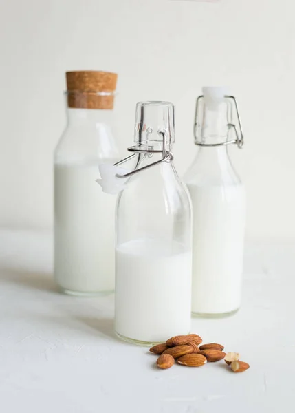 Cow or nut milk in a glass and bottles on white table in the kitchen.