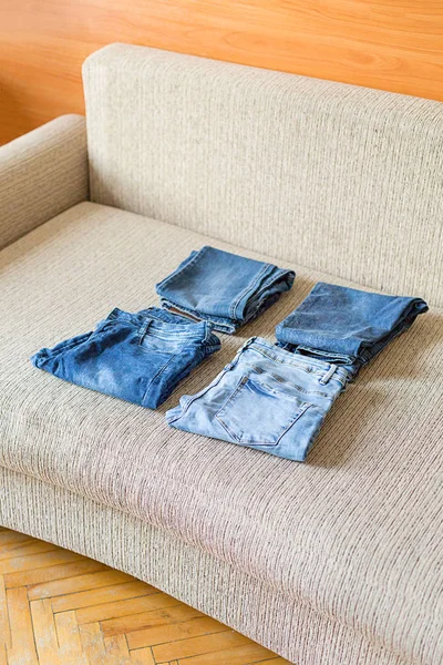 Several folded denim clothes are on the sofa. Shades of blue denim fabric.