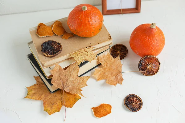 Sonbahar bileşimi kuru sarı akçaağaç yaprakları, Turuncu kabak ve beyaz arka plan üzerinde eski kitaplar
