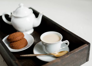 Çay seti, çikolata yulaf ezmeli kurabiye, İngilizce çay veya sütlü kahve koyu ahşap tepsi. Arka plan beyaz, uzay kopyalayın. Kahvaltı konsepti.