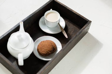 Çay seti, çikolata yulaf ezmeli kurabiye, İngilizce çay veya sütlü kahve koyu ahşap tepsi. Arka plan beyaz, uzay kopyalayın. Kahvaltı konsepti.