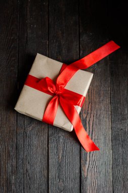 Bir hediye kutusu kraft kağıt, el yapımı, kırmızı kurdele, koyu ahşap arka plan. Tatil kavramı