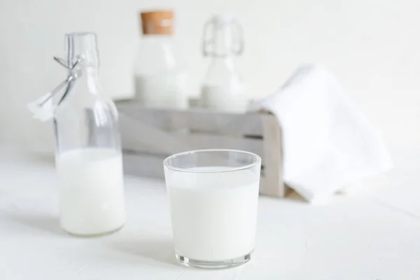 Fresh milk in bottles and glass on white concrete background. Healthy food, kitchen.