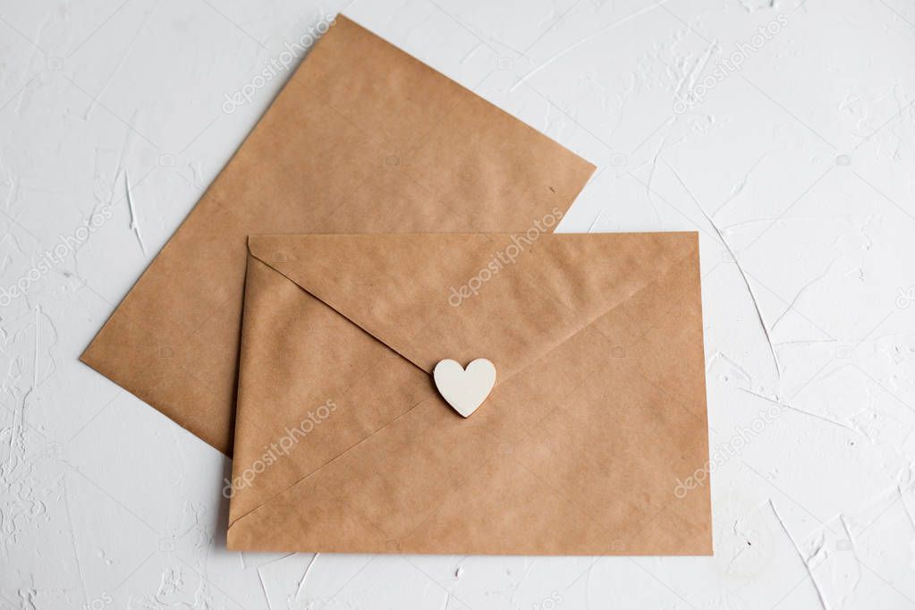 Top view of a letter to a beloved person. Kraft paper envelope, wooden small hearts and a shift of paper on white table.