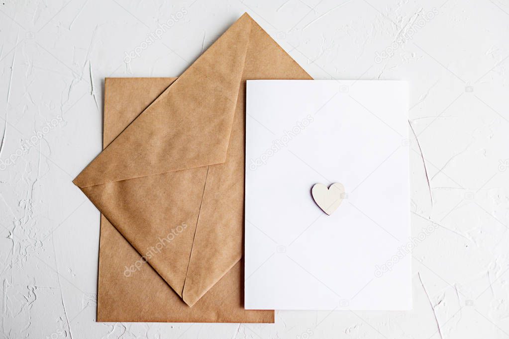 Top view of a letter to a beloved person. Kraft paper envelope, wooden small hearts and a shift of paper on white table.