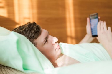 Genç bir adamla yatakta bir akıllı telefon mesajlarını erken sabah elinde.