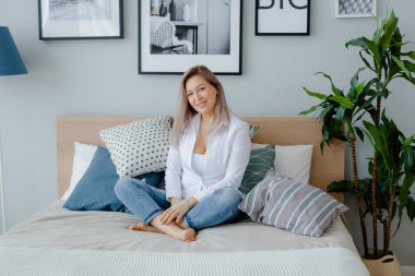 Bir kadın büyük yatakta oturuyor.