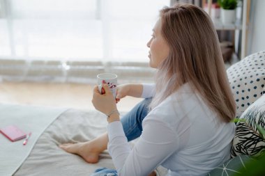 Sarışın genç kadın dizüstü bilgisayar ile yatakta oturur