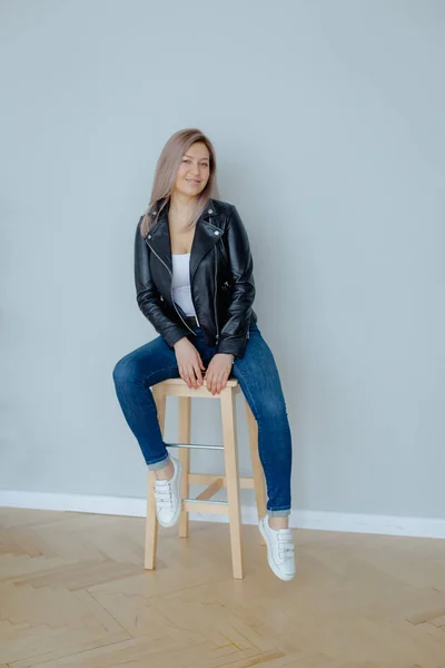 Una mujer rubia con una chaqueta de cuero negro está sentada — Foto de Stock